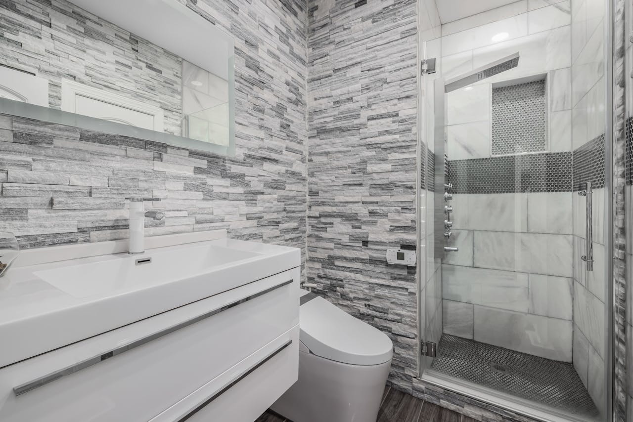 Stylish modern bathroom featuring a glass shower, stone walls, and sleek white vanity.